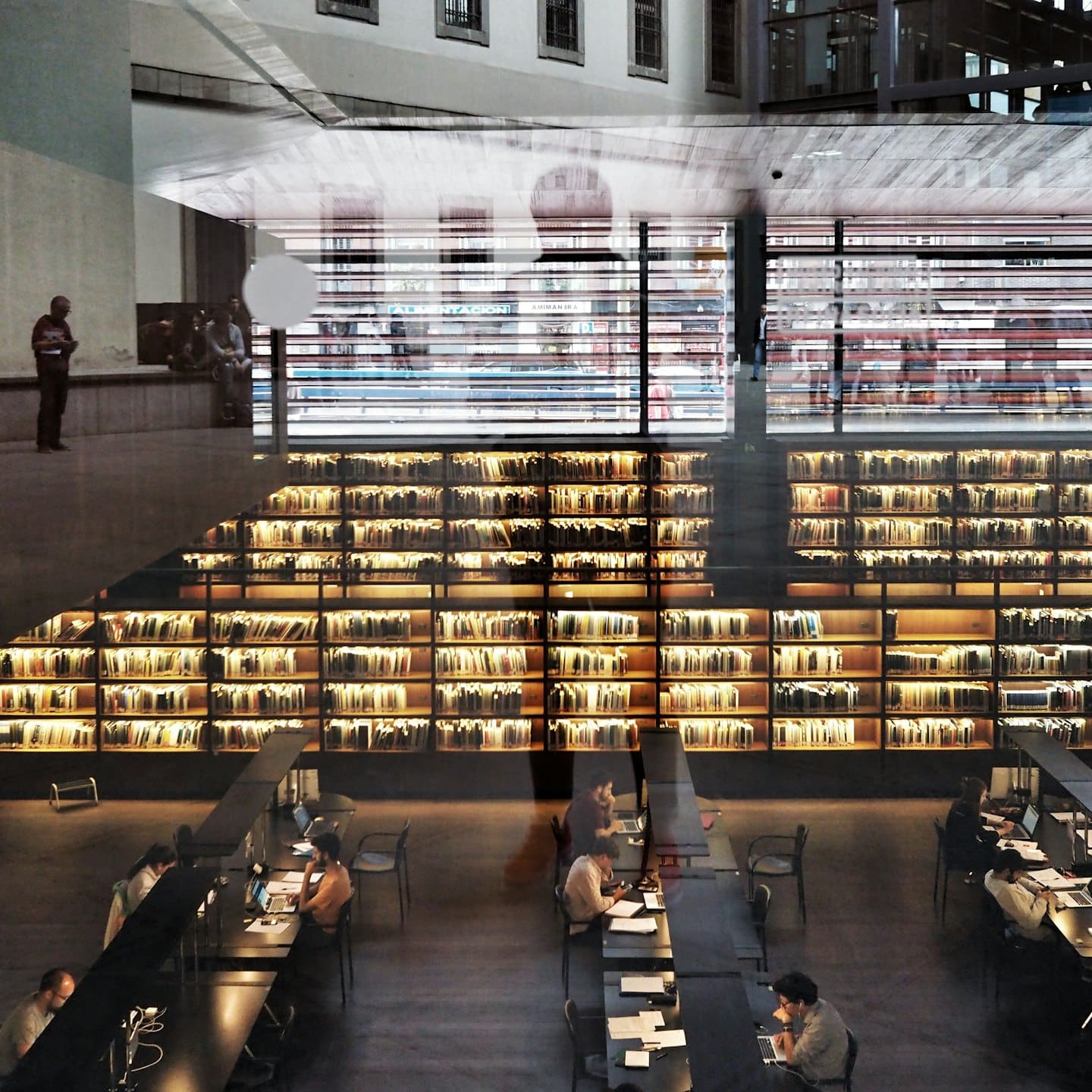 Persone che studiano e lavorano in una biblioteca moderna con molte librerie.